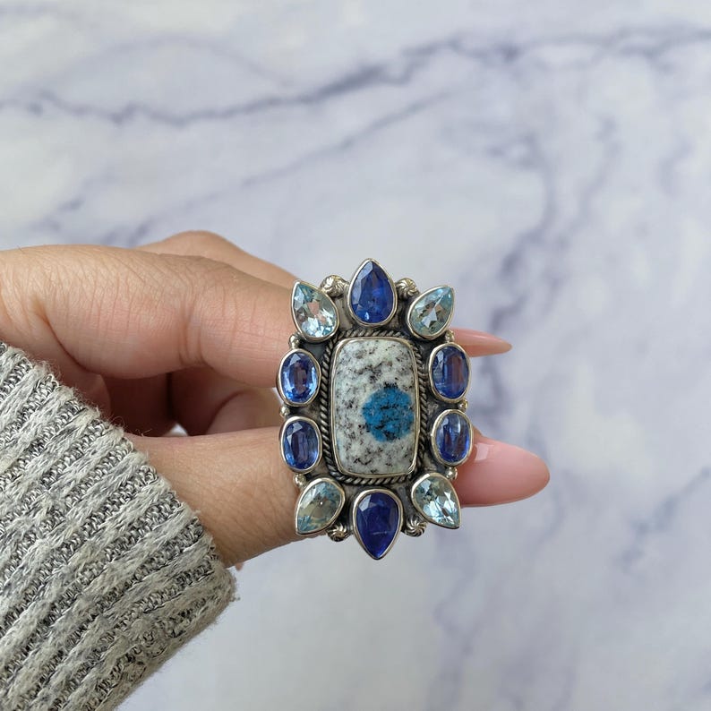 May include: A silver ring with a large rectangular blue and white stone surrounded by smaller blue and light blue stones.