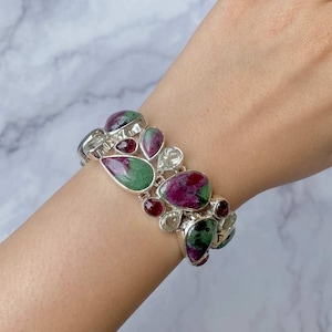 May include: A silver bracelet with green and pink gemstones. The bracelet is made of sterling silver and features a variety of gemstones, including green and pink.