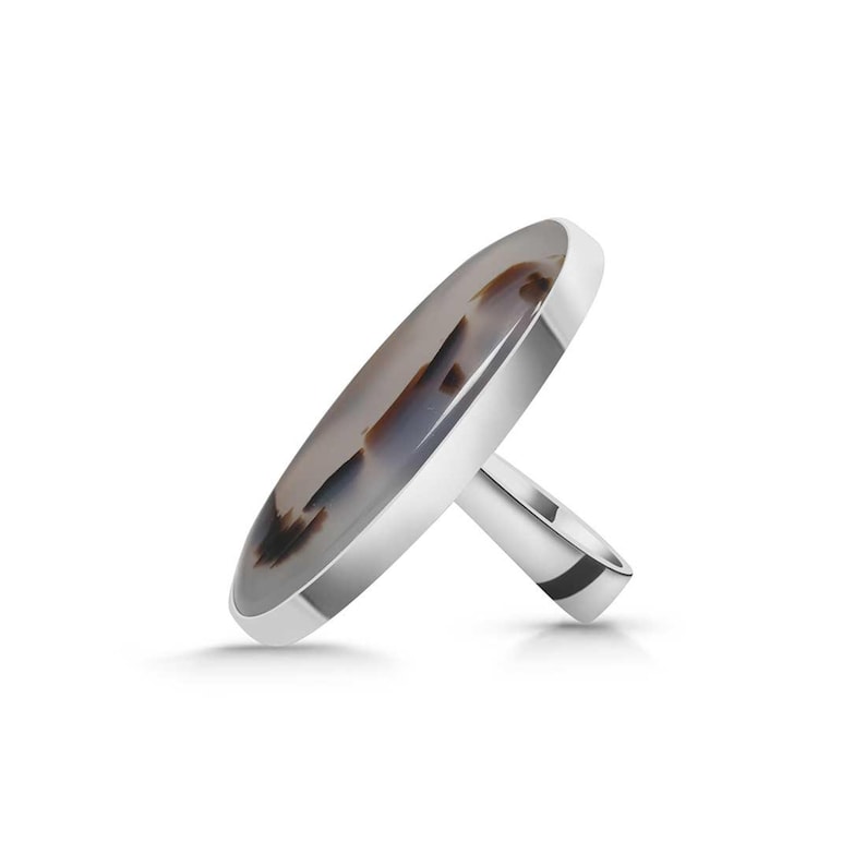 May include: A silver ring with a large oval agate stone set in the center. The agate is a light gray color with brown and black markings.