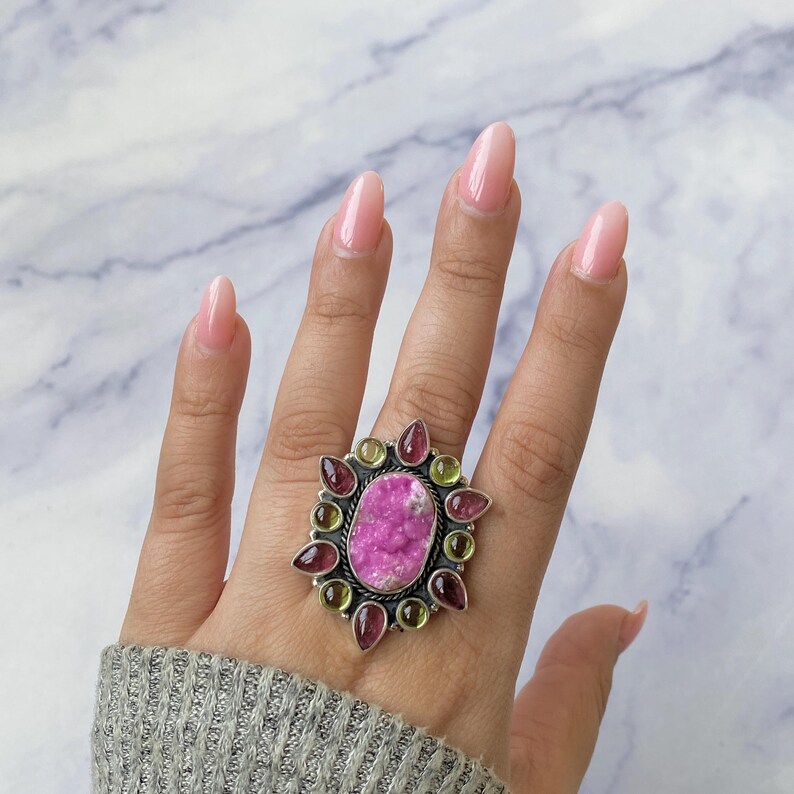 May include: A silver ring with a pink and green gemstone surrounded by smaller pink and green gemstones.