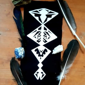 Könnte beinhalten: Schwarzer Stoff-Patch mit einem weißen geometrischen Design. Das Design besteht aus fünf Diamantenformen, jede mit einem anderen Muster. Der Patch ist von Federn und Steinen umgeben.