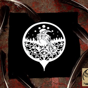 Op de afbeelding: Een zwart-witte patch met een gestileerde afbeelding van een vogel met een groot oog in het midden van een cirkel. De vogel zit op een tak met een bos erachter. De cirkel is omgeven door een ring van sterren en manen.