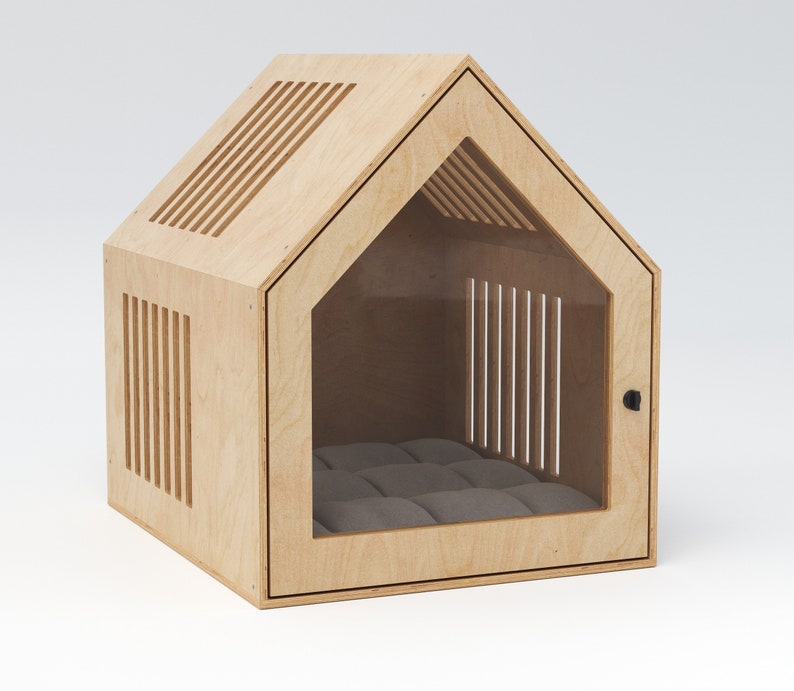 May include: A light-colored wooden pet house with a house-shaped design. The structure features ventilation slots and a clear door, revealing a gray cushion inside. A small black latch secures the door.