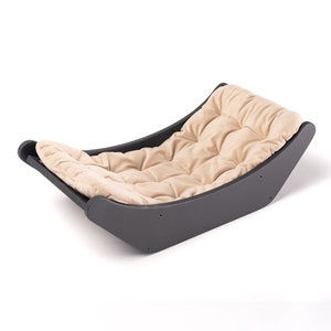 May include: A black wooden pet bed with a beige cushion. The bed is curved and has a rounded shape. The cushion is soft and comfortable.