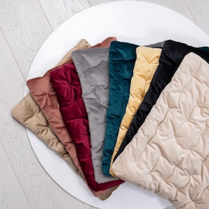 Pode incluir: Uma coleção de almofadas de veludo acolchoadas em várias cores, incluindo bege, rosa, bordô, cinza, verde-azulado, amarelo, preto e creme. As almofadas estão dispostas em forma de leque sobre uma superfície branca, mostrando sua textura macia e tons ricos.