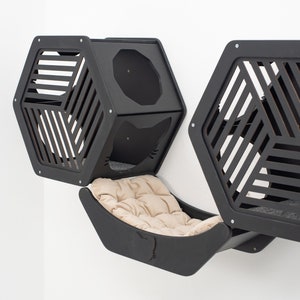 May include: Black cat condo with a hexagonal design and a hammock bed. The condo has two separate compartments with a slatted design and a round opening. The hammock bed is attached to the condo and has a beige cushion.