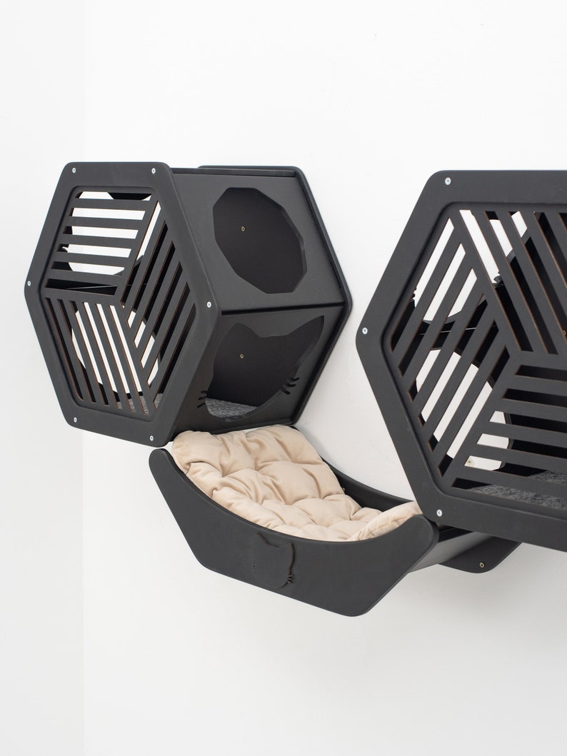 May include: Black cat condo with a hexagonal design and a hammock bed. The condo has two separate compartments with a slatted design and a round opening. The hammock bed is attached to the condo and has a beige cushion.