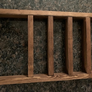 Puede incluir: Una estantería de madera rústica con cuatro compartimentos abiertos. La estantería está teñida de un color marrón oscuro y tiene una veta de madera natural.
