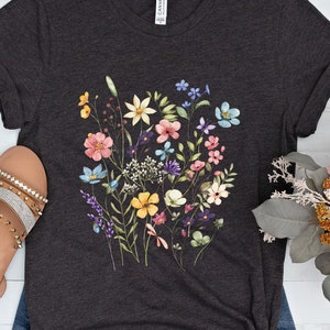 May include: A dark heather grey t-shirt with a floral print featuring a variety of colorful flowers, including pink, yellow, blue, and purple.