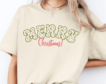 May include: A beige t-shirt with a green, red, and white "Merry Christmas!" graphic featuring a pattern of Christmas trees.