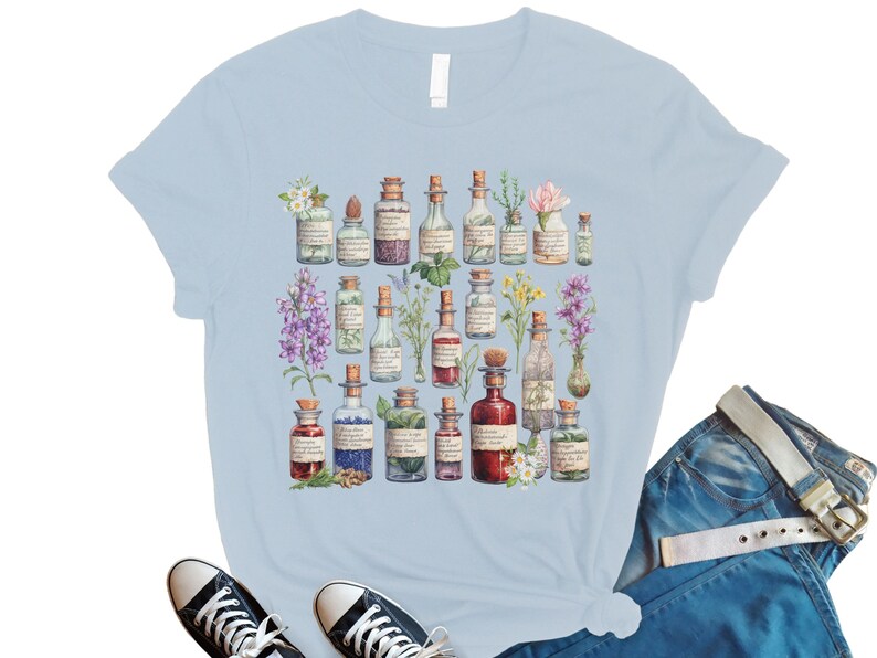May include: Light blue t-shirt with a vintage illustration of various glass bottles filled with colorful liquids and flowers. The bottles have labels with handwritten text.