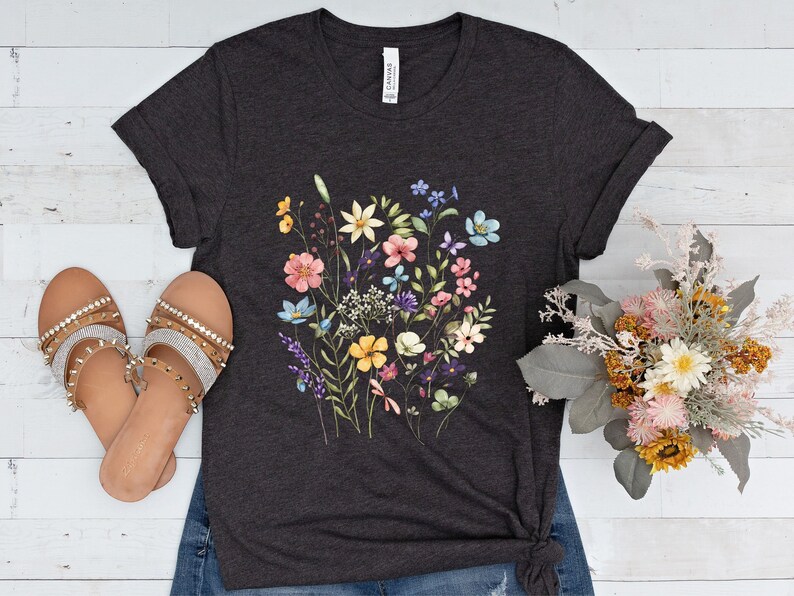 May include: A dark heather grey t-shirt with a floral print featuring a variety of colorful flowers, including pink, yellow, blue, and purple.