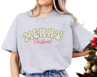 May include: A gray t-shirt with a festive design featuring the words "Merry Christmas!" in a retro font. The letters are filled with a pattern of colorful Christmas trees.