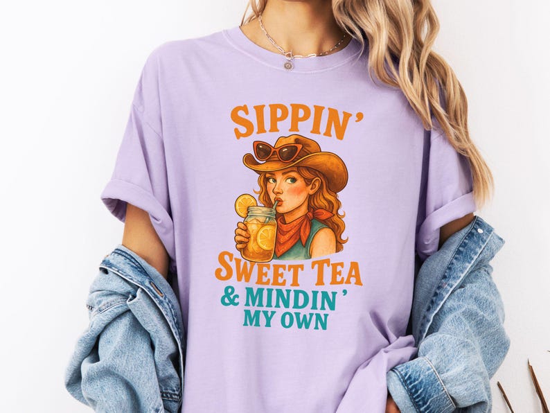 May include: A purple t-shirt with the text "Sippin' Sweet Tea & Mindin' My Own" and a cartoon illustration of a woman wearing a cowboy hat and sunglasses, drinking a glass of iced tea.