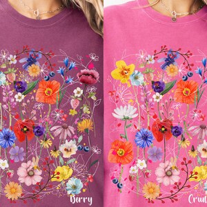 May include: Two pink and purple t-shirts with a floral design. The design features a variety of flowers in shades of pink, red, yellow, blue, and green. The text "Barry" is printed on the left shirt and "Crunchberry" is printed on the right shirt.