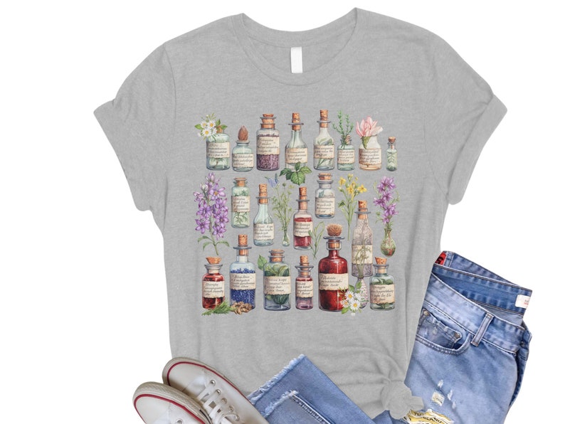 May include: A gray t-shirt with a design of various glass bottles filled with colorful liquids and herbs. The bottles are surrounded by flowers and leaves.