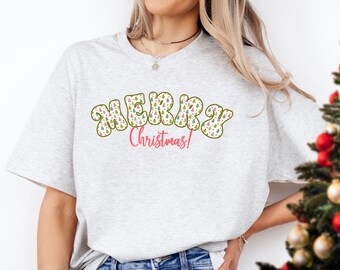 May include: A gray t-shirt with a festive design featuring the words "Merry Christmas!" in a retro font with a pattern of colorful Christmas trees.