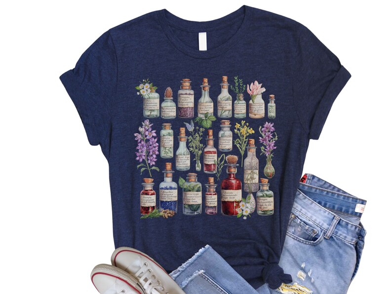 May include: A navy blue t-shirt with a graphic print of various glass bottles filled with colorful liquids and herbs. The bottles are arranged in a circular pattern and have labels with handwritten text.