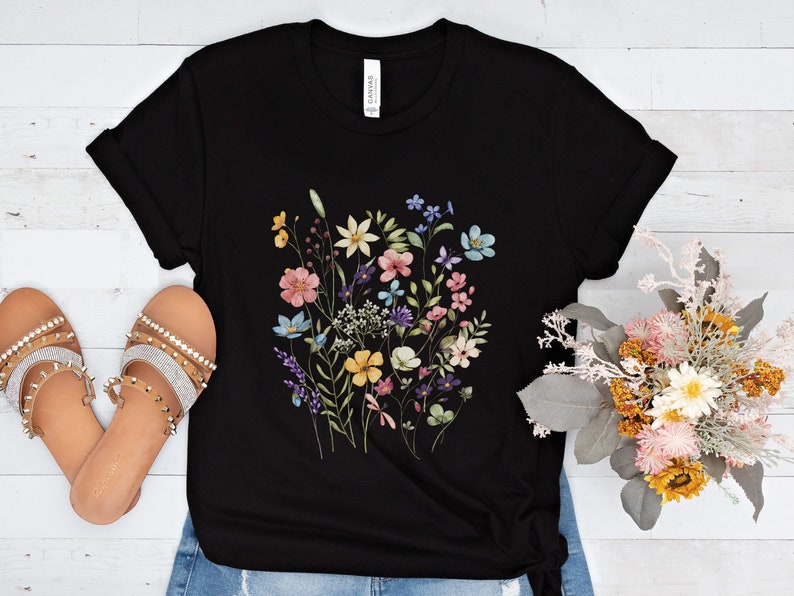 May include: Black t-shirt with a colorful floral print featuring pink, yellow, blue, and green flowers.
