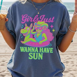 May include: Blue t-shirt with a graphic of a woman in a swimsuit and sunglasses floating on a pool float with a cartoon donkey. Text reads "Girls Just Wanna Have Sun" in pink and green.