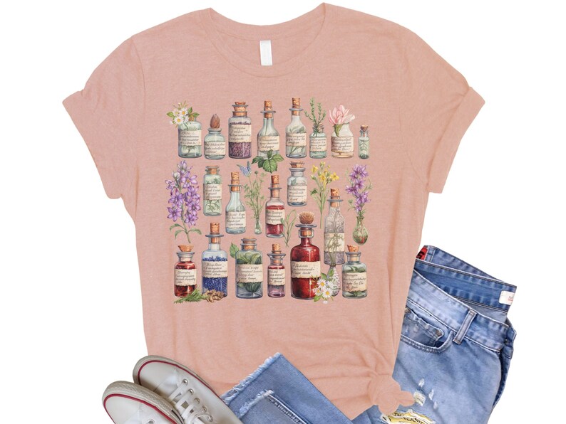May include: A pink t-shirt with a floral design featuring a variety of glass bottles filled with colorful liquids. The bottles are surrounded by flowers and leaves. The design is reminiscent of a vintage apothecary.