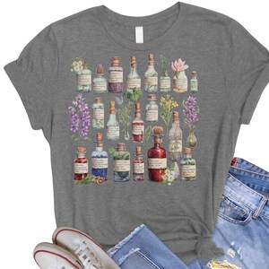 May include: A heather gray t-shirt with a vintage illustration of various glass bottles filled with colorful liquids and surrounded by flowers and herbs.