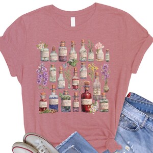 May include: A dusty rose t-shirt with a vintage illustration of various glass bottles filled with colorful liquids and topped with different flowers and herbs.