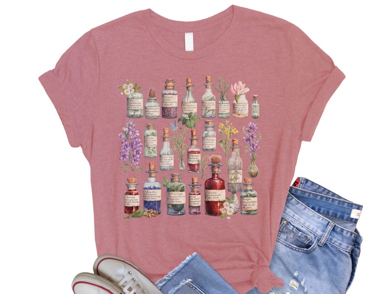 May include: A dusty rose t-shirt with a vintage illustration of various glass bottles filled with colorful liquids and topped with different flowers and herbs.