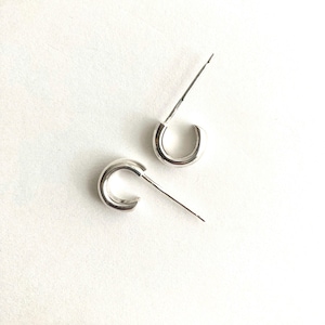 May include: A pair of small, polished silver-tone hoop earrings with a smooth, rounded profile. Each earring features a thin, straight post extending from the top of the hoop, designed for secure attachment to the earlobe with a simple, clean aesthetic.
