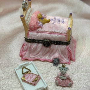 以下が含まれることがあります： 「THE PRINCESS SLEEPS HERE」と書かれたピンクのキルトが付いたベッド型のミニチュア小物入れ、小さなテディベア、「THE PRINCESS HANDBOOK」というタイトルの本が乗った白いトレイ、ピンクのドレスを着た小さなネズミのフィギュア。