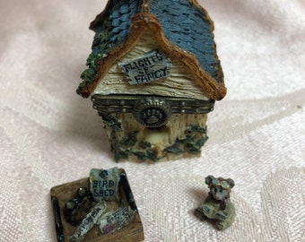 May include: A miniature ceramic birdhouse with a blue roof and a sign that reads "Flights of Fancy". There is a small wooden tray with a bird seed bag and a miniature bear wearing goggles and holding a map.