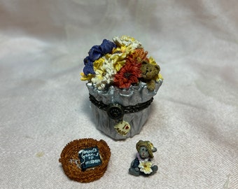 May include: A silver trinket box shaped like a trash can with a bouquet of flowers and a teddy bear peeking out. The box has a small heart charm that says "I love you". There is a small brown wicker basket with a book that says "Grandma's Book of Wisdom" and a small teddy bear holding a flower.