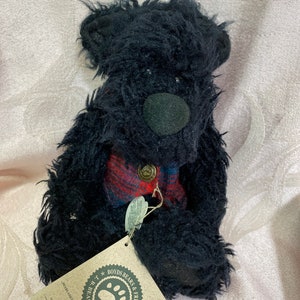 Può includere: Un orsacchiotto di peluche nero con pelo arruffato, un naso in feltro scuro e un gilet a quadri rossi e blu con un bottone in ottone. È attaccata un'etichetta di cartone beige con il testo Boyds Bears & Friends J.B. Bean & Associates.