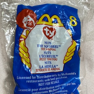 May include: A blue and yellow McDonald's Happy Meal bag with a Ty Beanie Baby toy inside. The bag features the Ty logo and the words "NUTS THE SQUIRREL TM TOY ANIMAL" in white text. The bag also has the number 8 printed on it.