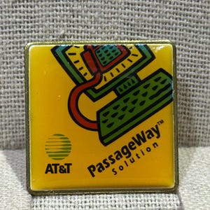 May include: A square, yellow pin with a gold border featuring a computer graphic in green, red, and black. The pin includes the AT&T logo and the text "PassageWay Solution."