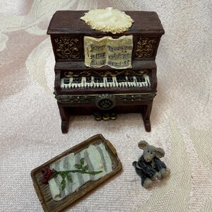 以下が含まれることがあります： 楽譜の付いたミニチュアの茶色のピアノ、バラの付いた小さなトレイ、小さなネズミの置物。 ピアノは装飾的な上部と白黒の鍵盤を備えています。 トレイはストライプのデザインです。