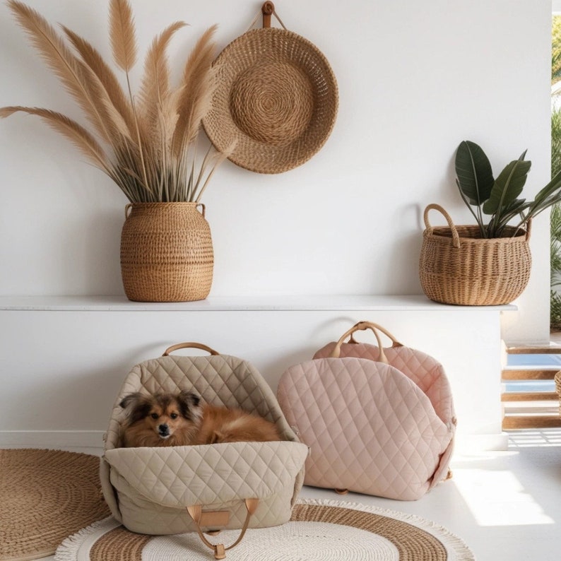 K&ouml;nnte beinhalten: Zwei gesteppte Haustierbetten, eines beige und eines rosa, stehen auf einer wei&szlig;en Oberfl&auml;che mit einem Weidenkorb und einem gewebten Wandbehang.