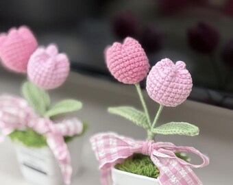 May include: Two pink crocheted tulip flower arrangements in white pots with pink and white gingham ribbon. The pots have a label that says "Handmade".
