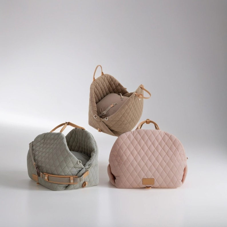 K&ouml;nnte beinhalten: Drei gesteppte Haustierbetten in verschiedenen Farben: Gr&uuml;n, Beige und Rosa. Die Betten haben ein gestepptes Design und sind aus weichem Stoff gefertigt. Die Betten haben Ledergriffe und -riemen.