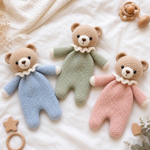 Può includere: Tre orsetti di peluche realizzati all'uncinetto con teste color marrone chiaro, occhi e nasi scuri, ognuno con un colletto bianco a balze. I corpi sono di colore azzurro, verde salvia e rosa tenue, con dettagli bianchi su mani e piedi.