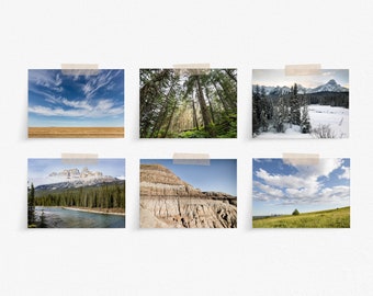 May include: Six landscape photographs, each taped to a white wall. The images depict diverse natural scenes: a blue sky over a field, a forest from below, snow-covered mountains, a mountain range over a river, a layered rock formation, and a grassy field.