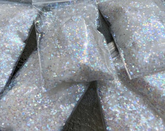 May include: Multiple small bags filled with iridescent white glitter. The glitter is loose and appears to be in a variety of sizes.