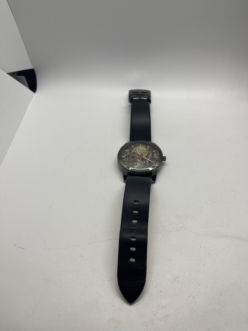 May include: A black leather wristwatch with a black face and silver hands. The watch has a black leather strap with a pointed end.