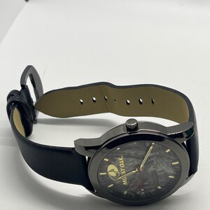 May include: Black leather wristwatch with a black face and a camouflage pattern. The watch face has a gold "MOssy OAK" logo.