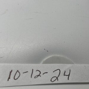 May include: A white surface with a piece of white paper taped to it. The paper has the date "10-12-24" written on it in black ink.