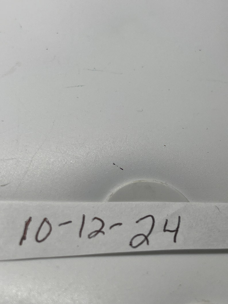 May include: A white surface with a piece of white paper taped to it. The paper has the date "10-12-24" written on it in black ink.