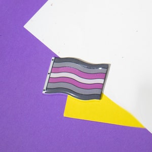 Op de afbeelding: Een grijze, witte en paarse vlag met golvende strepen. De vlag bevindt zich op een paarse en gele achtergrond.