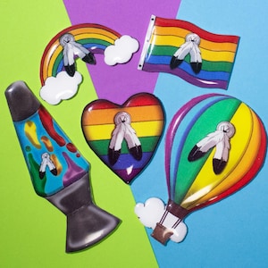 Könnte beinhalten: Fünf bunte, regenbogenfarbene, harzähnliche Ornamente mit einem indianischen Federdesign. Die Ornamente umfassen ein Regenbogenherz, eine Regenbogenflagge, einen Regenbogenbogen, einen Regenbogenluftballon und eine Regenbogen-Lavalampe.