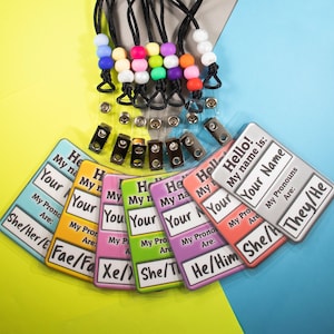 May include: Set of seven colorful name tags with clear plastic holders and lanyards. Each tag has a different pronoun set: She/Her/Hers, Fae/Faer/Faers, Xe/Xem/Xers, She/They/Them, He/Him/His, She/He/They, and They/Them/Their.