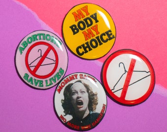 May include: Four round buttons with different messages and images. The first button is green and says "Abortion Save Lives" with a red outline of a coat hanger. The second button is yellow and says "My Body My Choice". The third button is white with a red outline of a coat hanger and says "Mommy Saves No More Wire Hangers". The fourth button is white with a red outline of a coat hanger and says "Mommy Saves No More Wire Hangers".